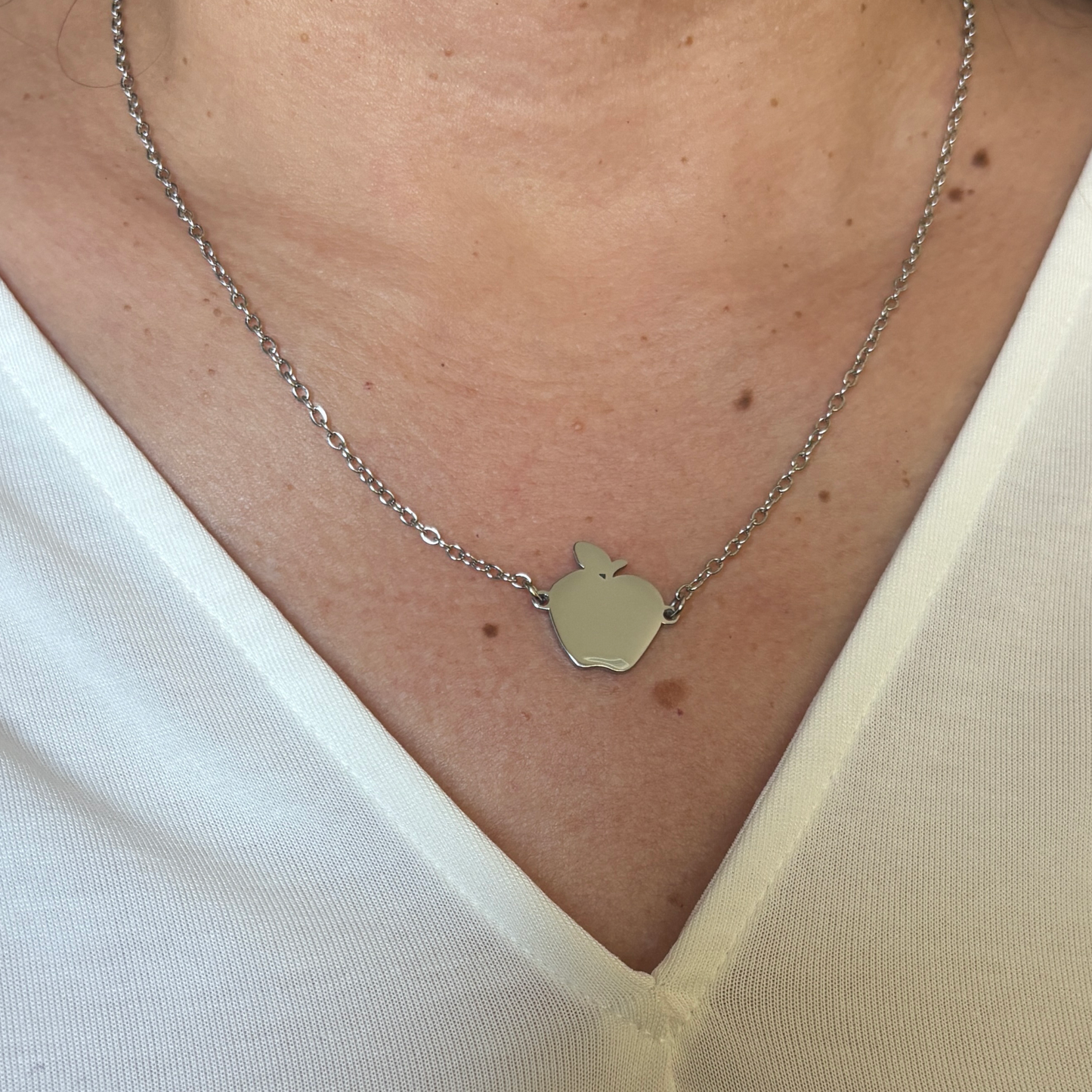 Woman wearing an apple shaped stainless steel necklace with a silver finish