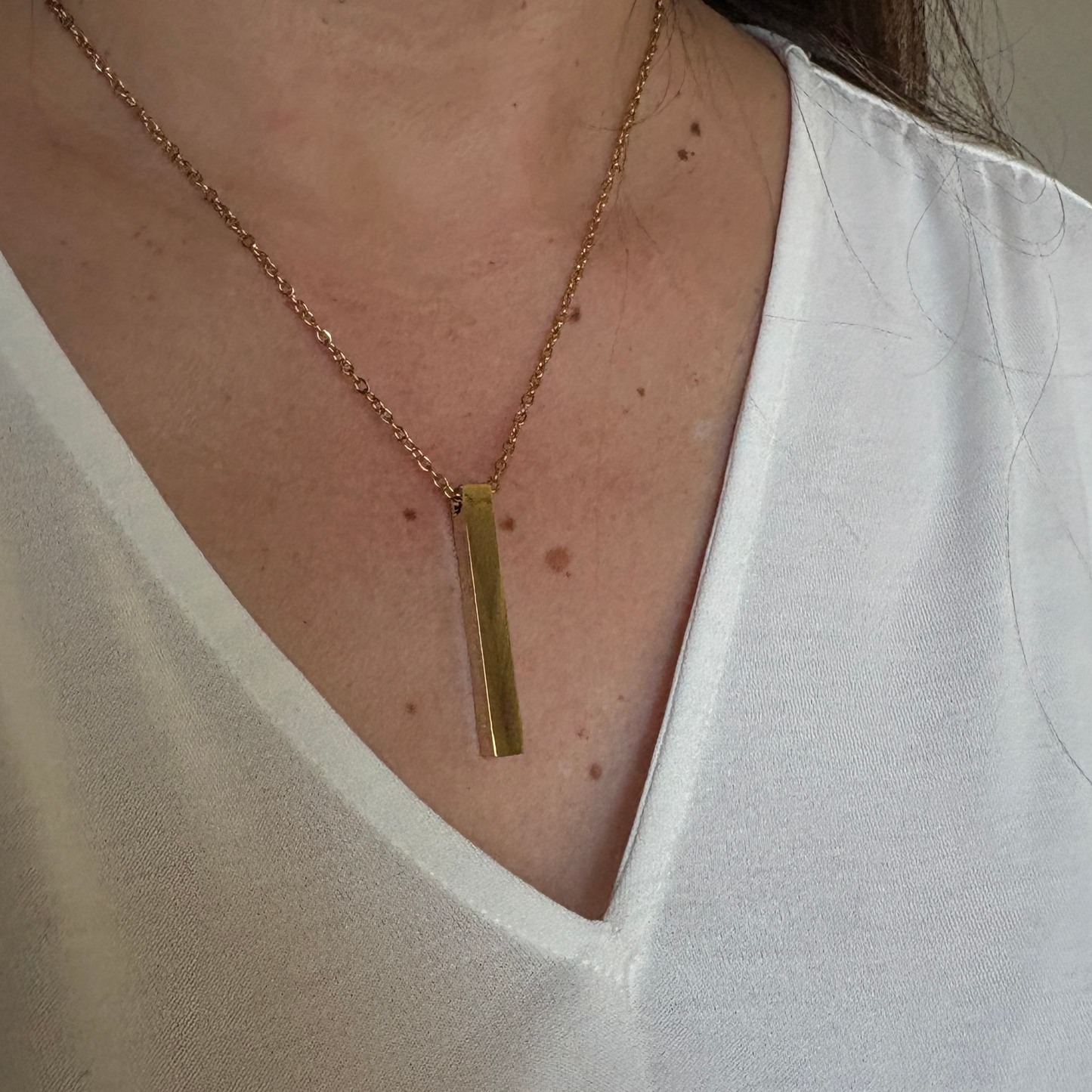 Woman wearing stainless steel gold vertical bar necklace.