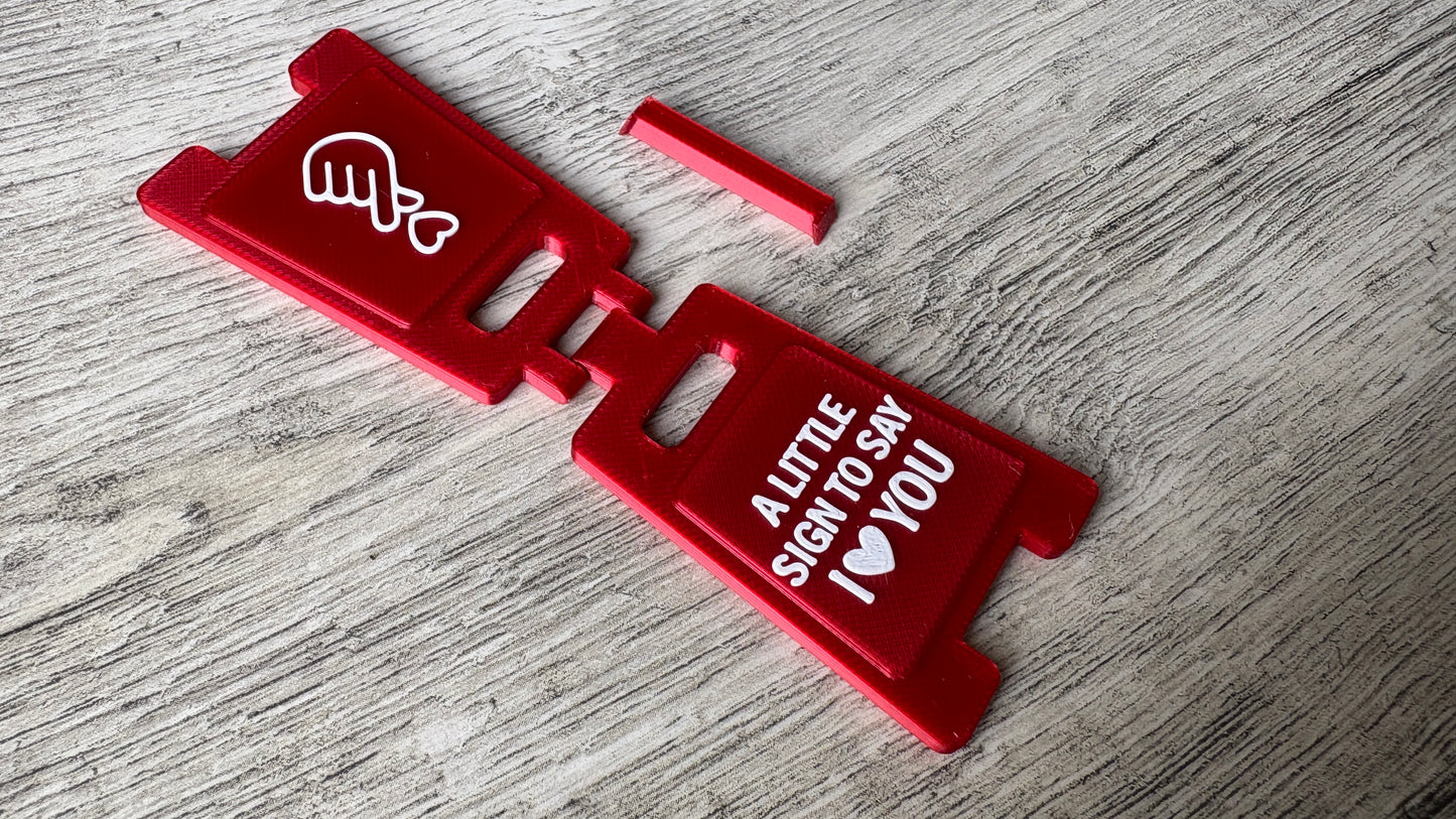 Unfolded 3D-printed mini sign with 'I love you' message & heart gesture laying flat.