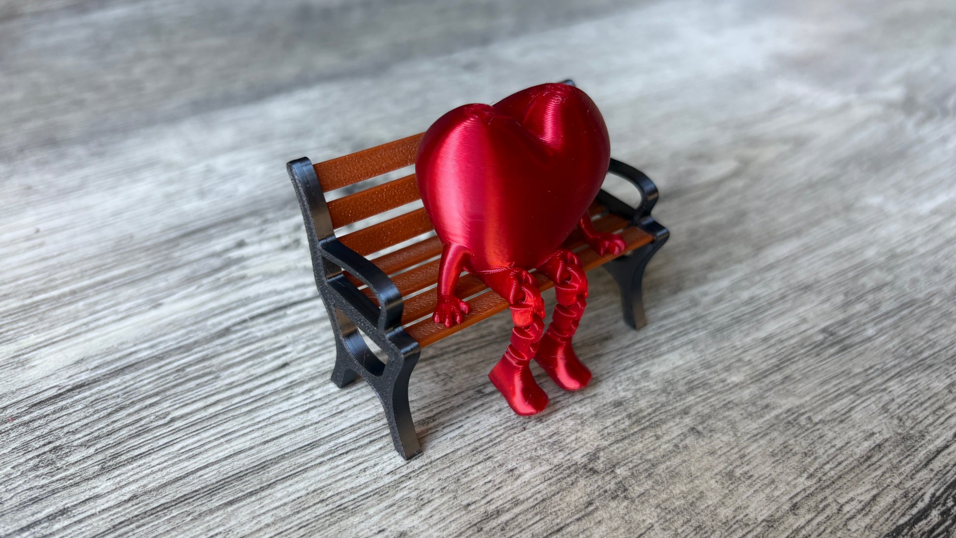 3D-printed heart with articulated legs that dangle playfully and is sitting in a bench