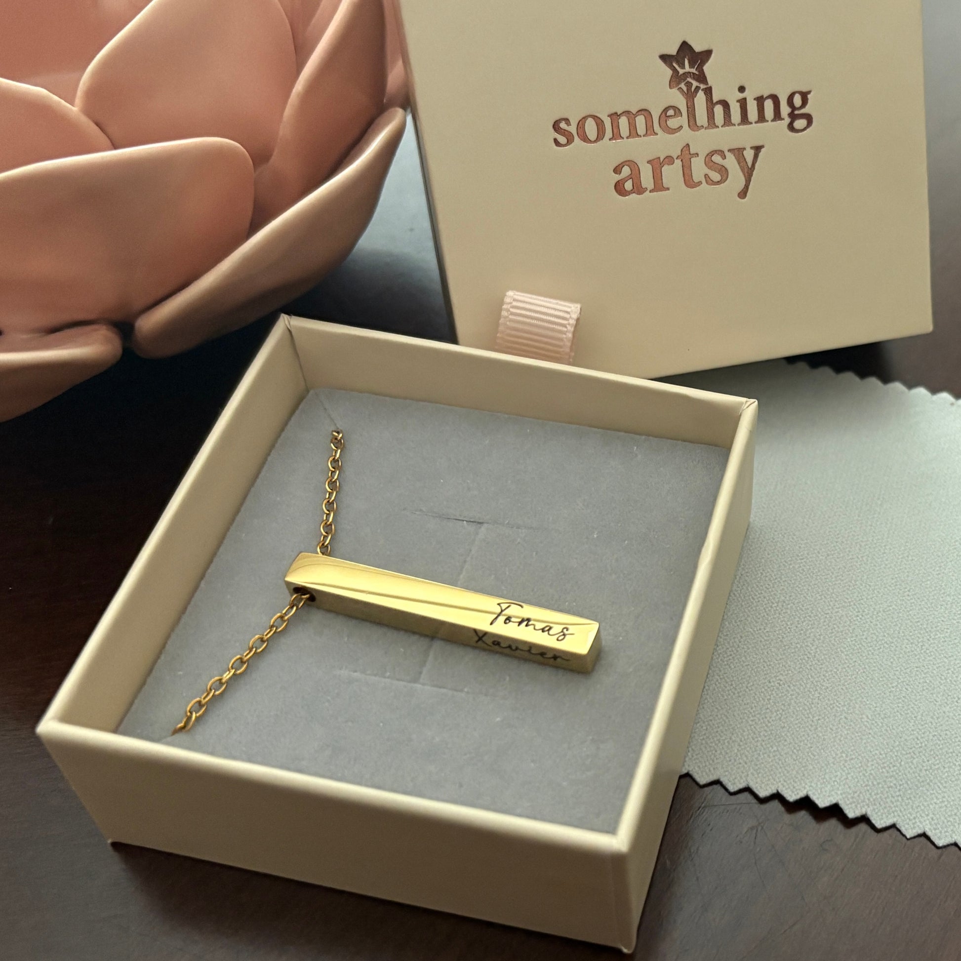 Gold necklace with a bar pendant engraved in a 'something artsy' box.