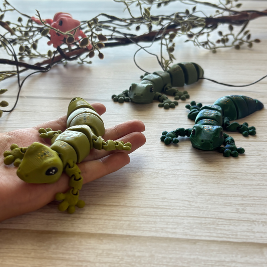 3D printed articulating gecko, one is being held by a hand while there are some that are a different color on the background