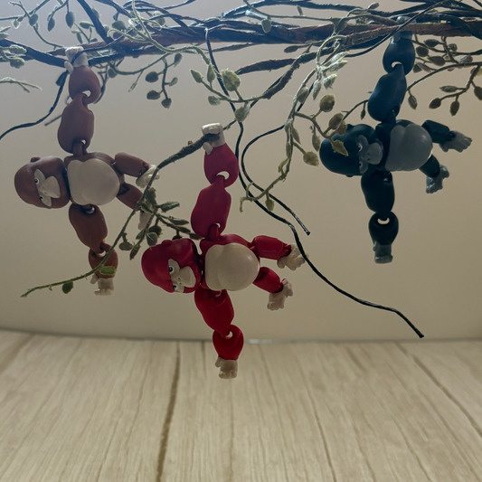 Hand-painted, 3D printed articulated gorilla hanging from a plastic plant with movable limbs, designed to hold hands with others and form a swinging chain.