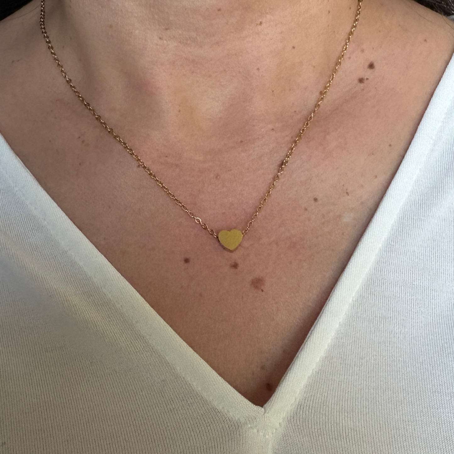 Woman wearing a stainless steel tiny heart charm  with a gold finish.