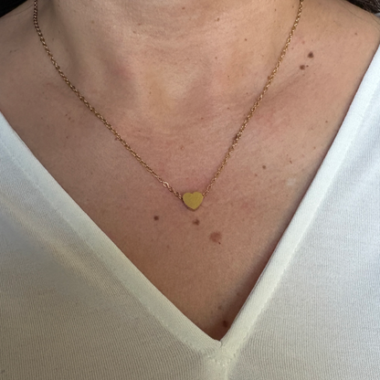 Woman wearing a stainless steel tiny heart charm  with a gold finish.