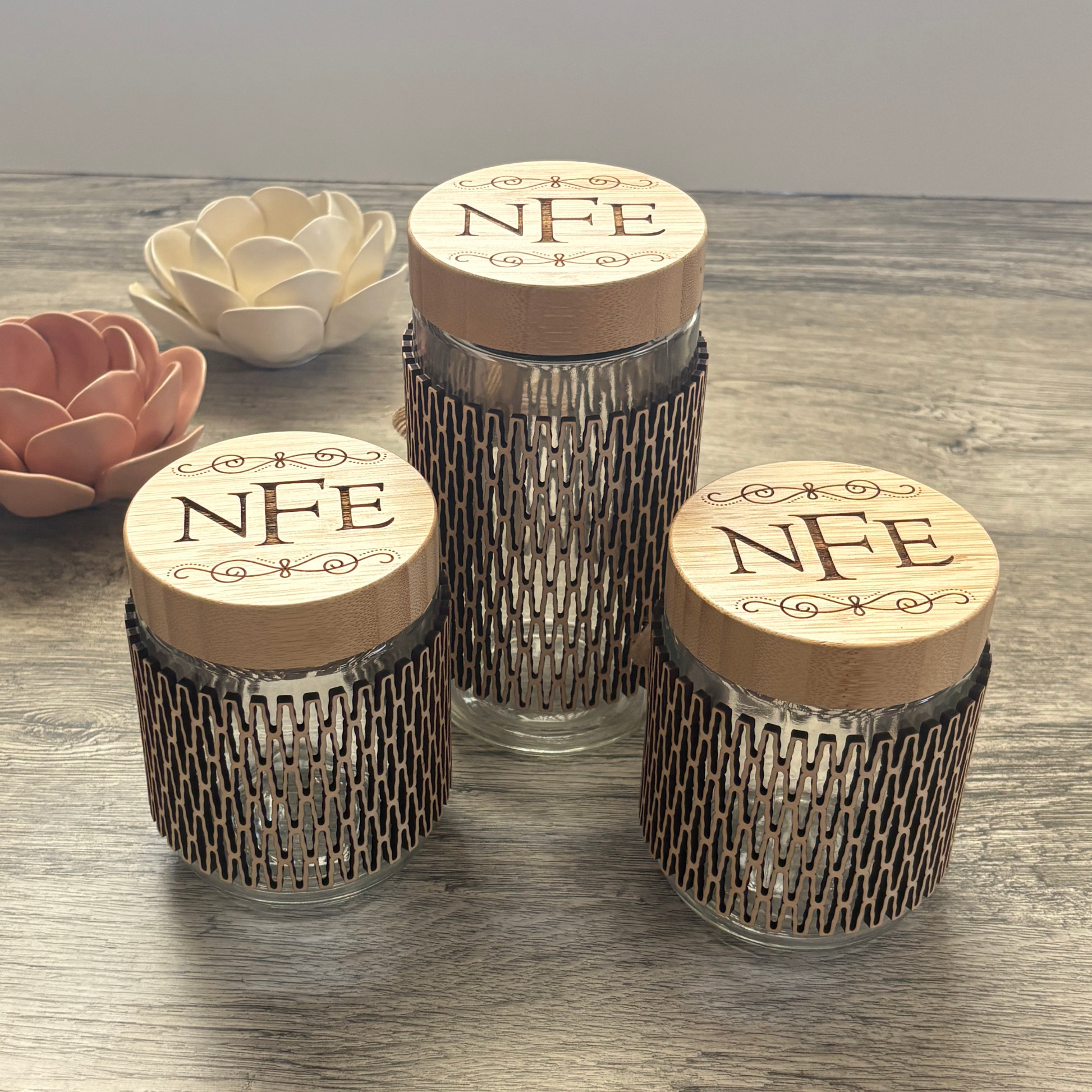 A 24oz and a 16oz glass jar that have custom engraving on bamboo lid and a wooden sleeve.