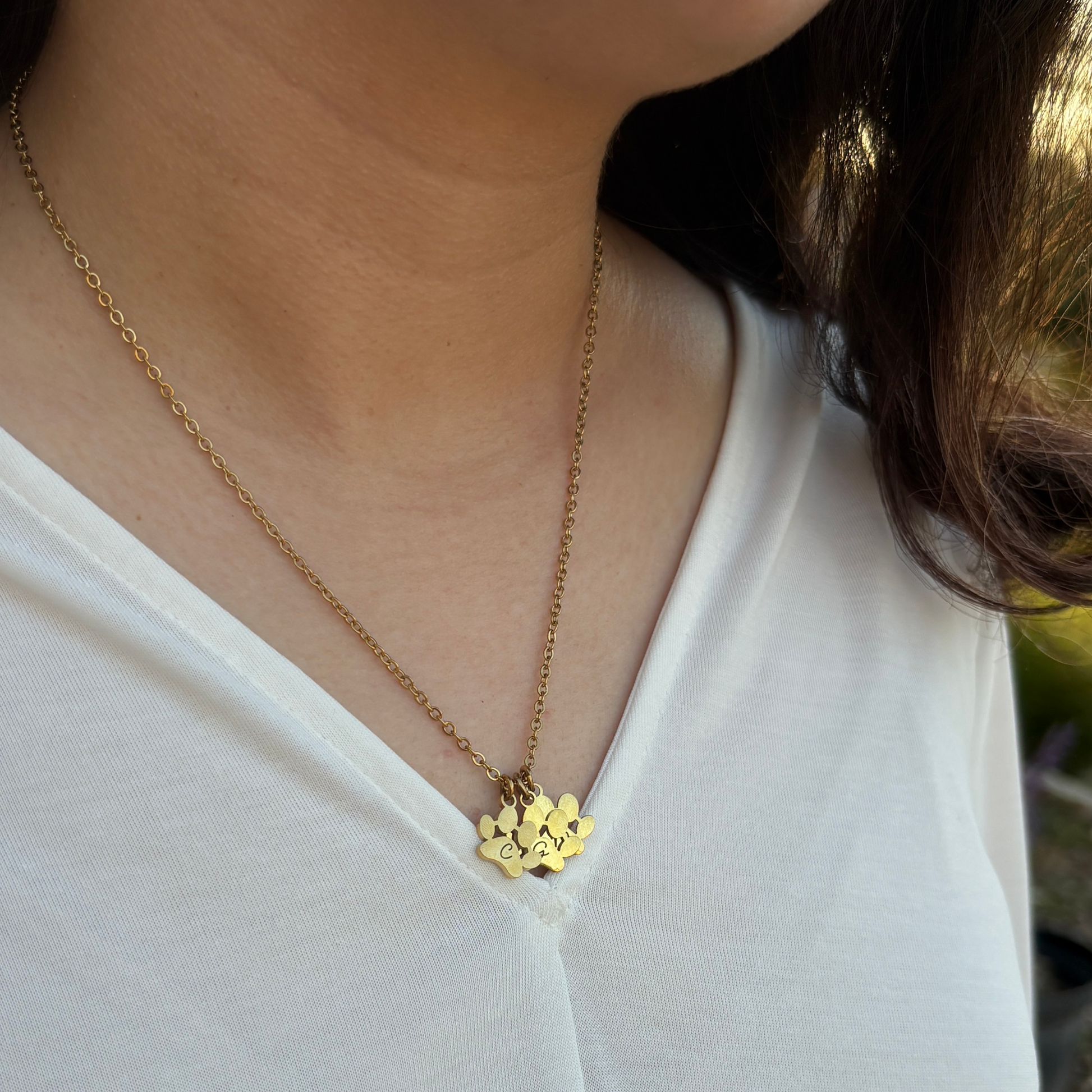 Someone wearing a gold necklace with 3 paw charms engraved with initials