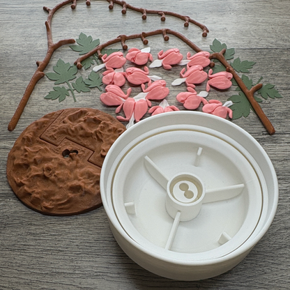 Unassembled 3D printed flowers, dirt, leaves, branches and a rotating storage that come together to assemble the Bleeding Hearts plant.