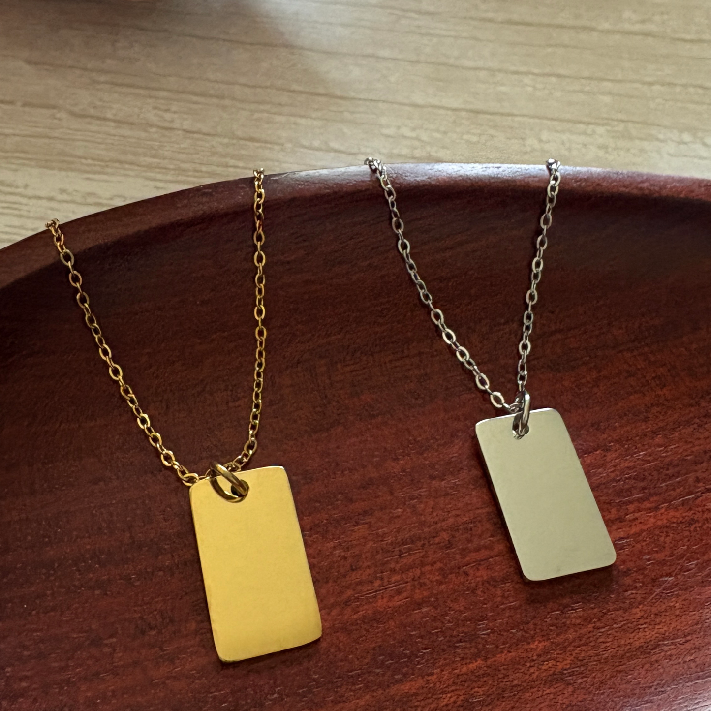 Small rounded rectangle stainless steel necklace in silver and gold on a wooden bowl